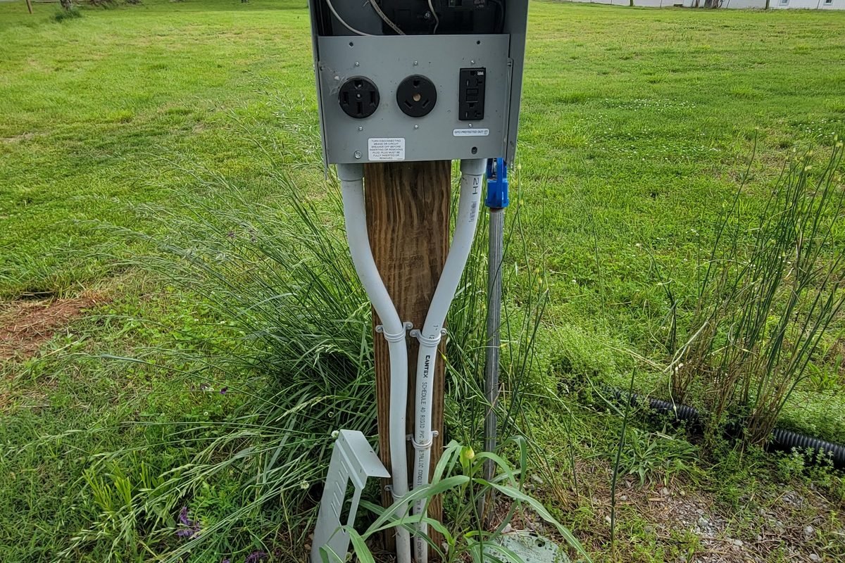 An electric meter base mounted on a utility pole at the edge of the field