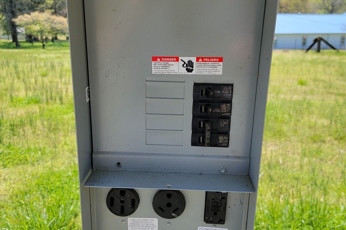 An open electrical panel mounted on a post in the field