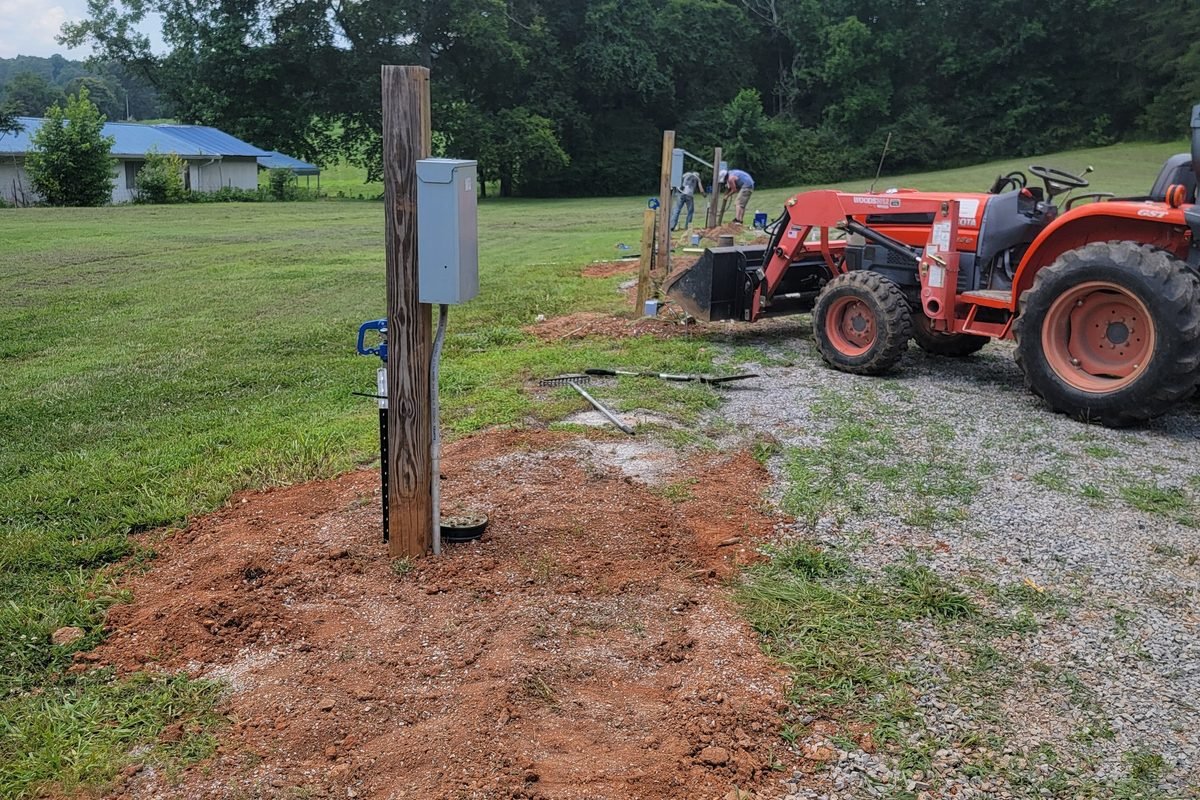 A utility pedestal post being set into freshly dug red clay