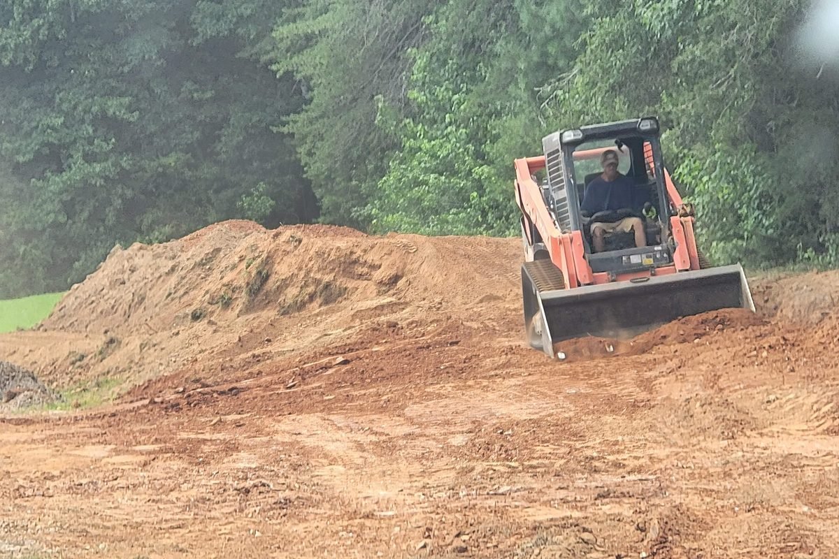 A skid steer moving a pile of dirt during site grading