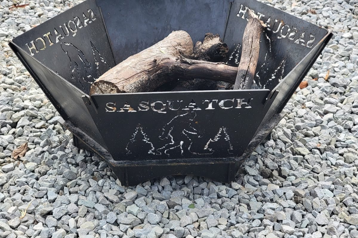 A black steel fire pit cut with a Sasquatch design, loaded with firewood