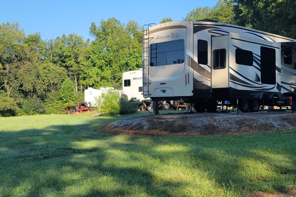 Two fifth wheels set up on their sites in morning light with trees behind