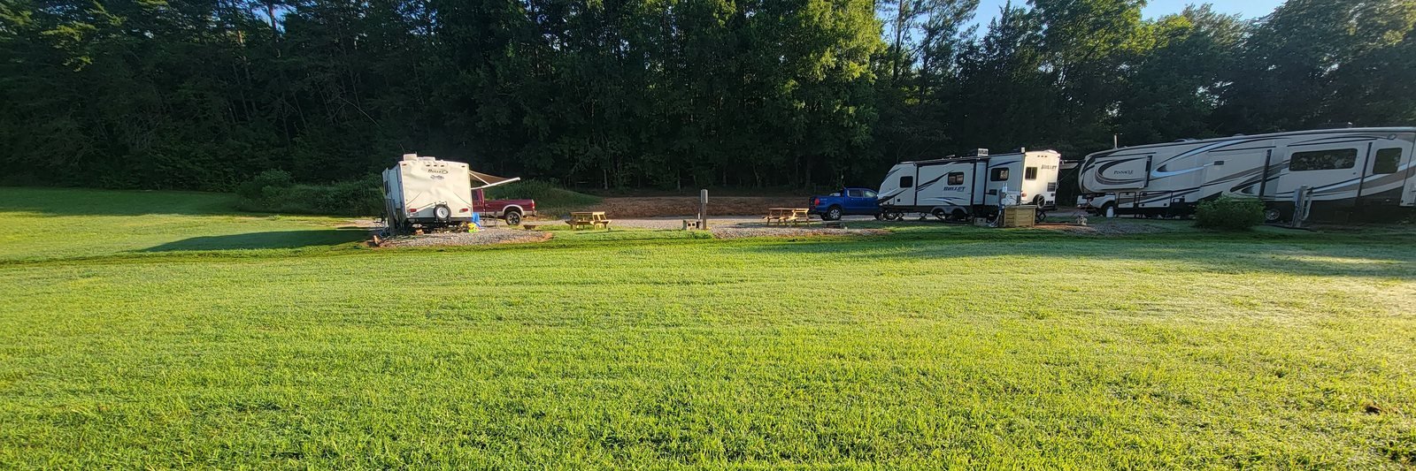 Gryptid RV Park in August 2026, RVs set up on their own well spaced sites along the treeline with open mowed lawn in front