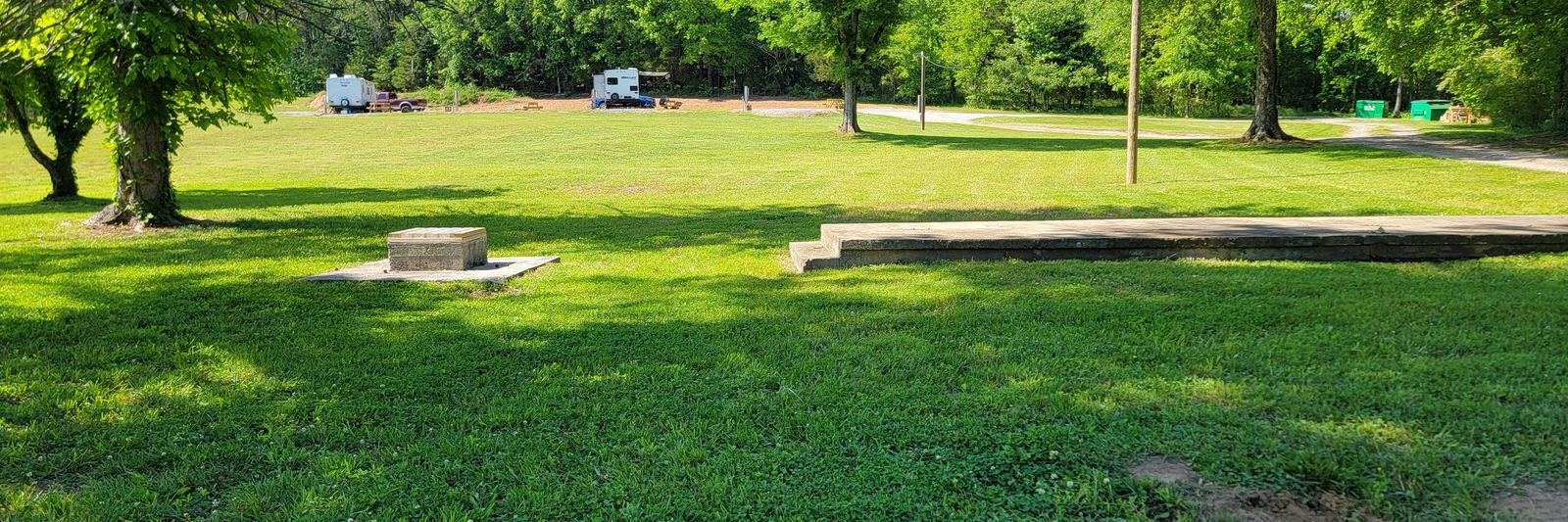 Open mown lawn at Gryptid RV Park framed by mature trees, with RVs parked at sites in the background